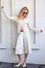 Woman in a white outfit posing against a light-colored wall.