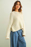 Woman wearing a cream knitted sweater and blue jeans against a plain background