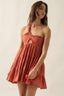 Woman wearing a rust-colored dress with cut-out design on a plain background