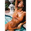 Woman in an orange bikini by a pool with decorative stone fountain in the background