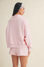 Person wearing a pink sweatshirt and shorts set on a beige background
