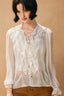 Woman wearing a white blouse with ruffled details against a beige background