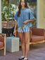 Woman wearing a denim shirt and striped shorts standing outdoors.