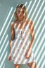 Woman wearing a white dress with sailboat pattern against a light blue wall.