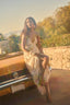 Woman in a floral dress sitting on the back of a vintage car with a scenic background