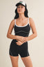 Woman wearing a black tank top and shorts with white trim on a beige background