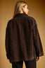 A woman shown from the back wearing an oversized dark brown corduroy jacket against a warm tan studio background.