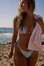 Woman in a bikini on a beach holding a pink towel