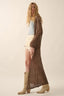 Woman wearing a long brown lace dress with beige boots on a plain background