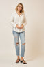 Woman wearing a white button-up shirt and light blue ripped jeans on a plain background