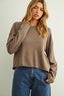 Woman wearing a brown sweater and blue jeans against a plain background
