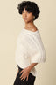 Woman wearing a textured white top against a beige background