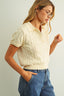 Woman wearing a cream-colored cable knit sweater and blue jeans against a plain background