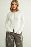 Woman wearing a white ribbed sweater and gray pants with bow patterns on a light background