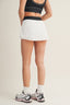 Person wearing a black sports bra and white skirt with black trim on a plain background