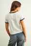 Woman wearing a white short-sleeve shirt with black trim and blue jeans on a light background