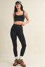 Woman wearing a black sports bra and leggings with hiking boots on a beige background