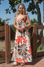 Woman wearing a floral dress standing outdoors near a wooden fence.