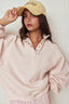 Woman wearing a light pink sweater and beige cap against a white background