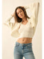 Woman wearing a cream knit cardigan and blue jeans against a plain background