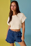 Woman wearing a white top and blue shorts against a multicolored background