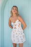 Woman wearing a white dress with sailboat pattern against a light blue wooden door.