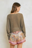 Woman wearing a green sweater and patterned shorts against a white wall