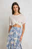 Woman wearing a white top with a knot detail and a blue floral skirt on a plain background