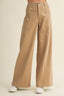 A person wearing high-waisted, wide-leg tan pants with white sneakers, shown from the waist down against a plain light beige studio background.