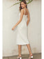 Woman wearing a white slip dress against a plain wall.