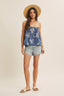 Woman wearing a blue top with white patterns and denim shorts on a beige background
