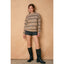 Woman wearing a striped sweater, shorts, and boots against a beige background