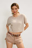 Woman wearing a beige t-shirt and shorts with a belt against a plain background