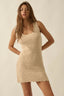 Woman wearing a beige crochet dress against a plain background