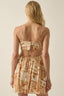 Woman wearing a patterned dress with thin straps on a beige background