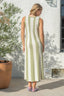 Woman wearing a green and white striped dress standing outdoors near a white wall.