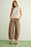 Woman wearing a white lace top and brown wide-leg pants on a light green background