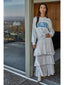 Woman wearing a gray sweatshirt with 'Malibu' text and a white layered skirt standing by a glass door.