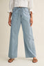 Person wearing light blue wide-leg jeans and a white blouse on a beige background
