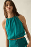 Woman wearing a teal sleeveless top and skirt set against a plain background