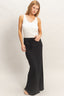 Woman wearing a white sleeveless top and black patterned skirt on a plain background