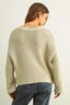 Person wearing a beige knitted sweater and blue jeans on a light background