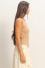 Woman wearing a beige sleeveless top and light-colored pants against a plain background