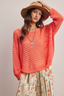 Woman wearing a coral sweater and beige hat against a plain background