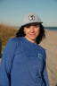 Woman wearing a blue shirt and gray cap with a palm tree logo on a beach.
