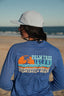 Person wearing a blue shirt with 'Palm Tree Island Wrightsville Beach' design on a beach.