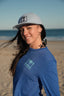 Woman wearing a blue shirt and gray cap with a palm tree design on a beach.